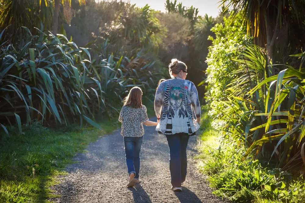 An adult and a child walking together on a gravel path, lined with foliage