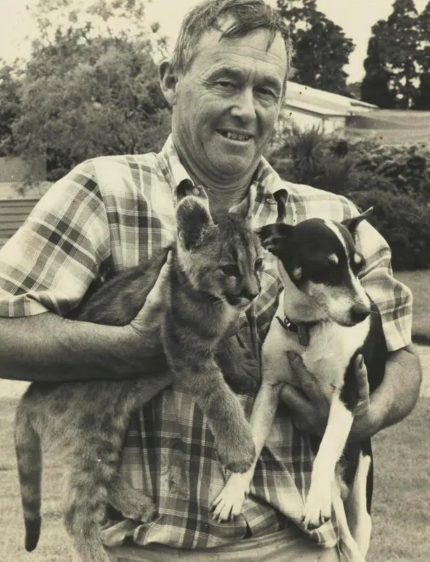 A man holding a puma cub and a dog